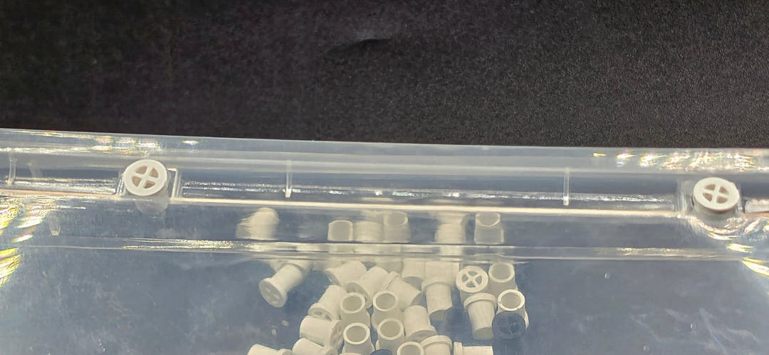 Two white vent plugs fitted through the wall of a clear plastic tub, with loose plugs inside it.