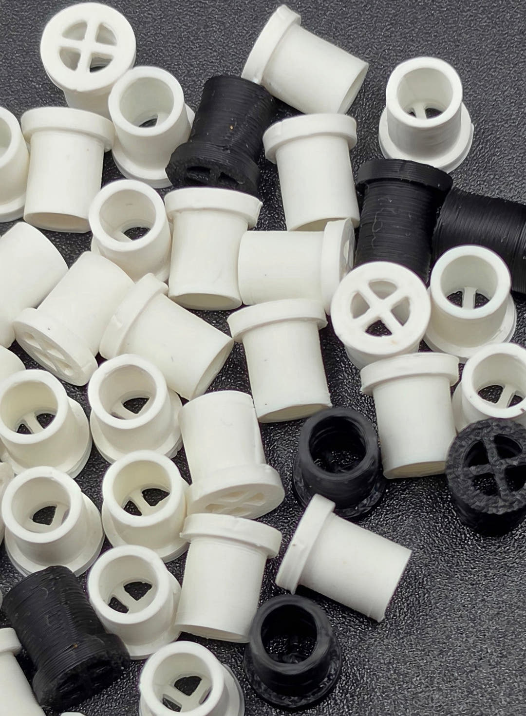 Close view of a jumbled pile of white and black vent plugs, some cross-slotted faces and some open tube ends.