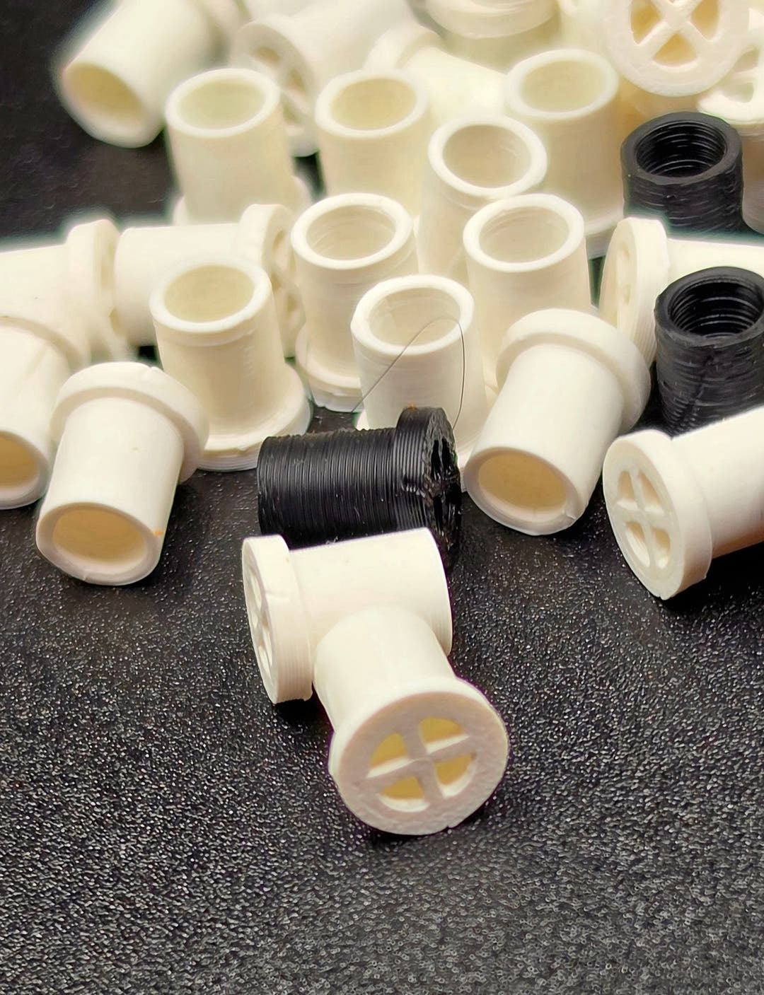 Cream vent plugs heaped with their open tube ends towards the camera, one lying face up by a black plug.