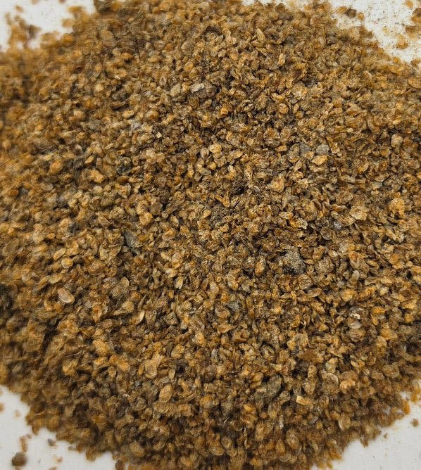 Dried daphnia piled on white, a coarse golden brown mix of small flattened flakes.