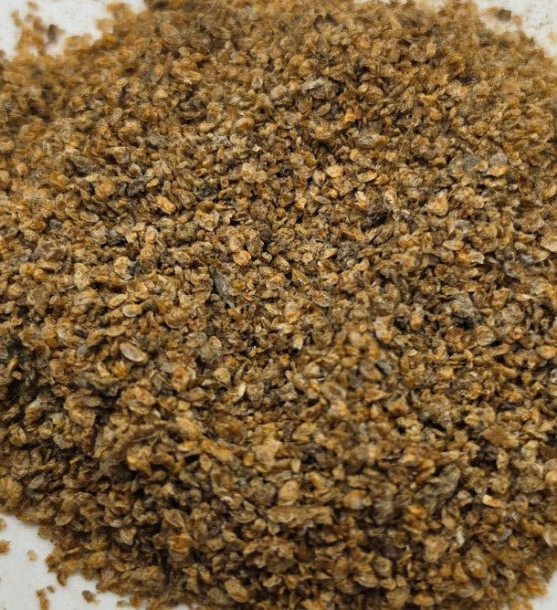 A mound of dried daphnia on a white surface, golden brown flakes with darker brown patches through it.