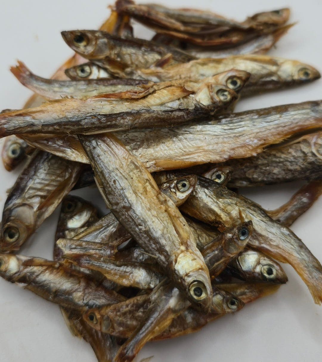 A heaped pile of dried sprats, silver and tan bodies with pale round eyes, filling the frame.