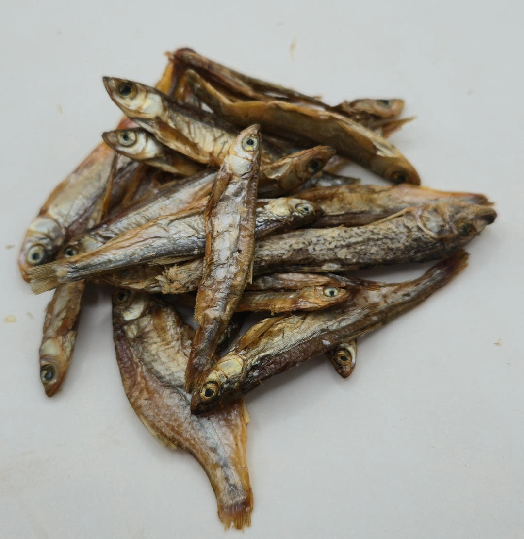 A small pile of dried sprats on a plain white surface, the whole heap visible with space around it.