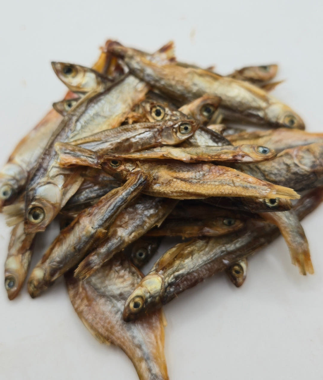 Dried sprats in a loose heap on white, one at the front lying with its tail fin spread wide.