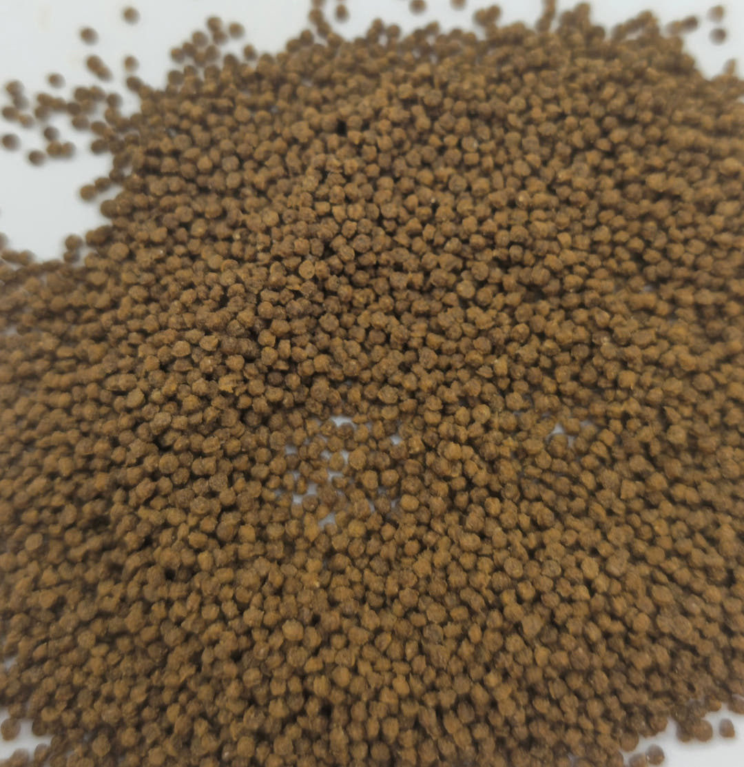 Brown insect granules poured into a loose mound, with white background showing at one corner.