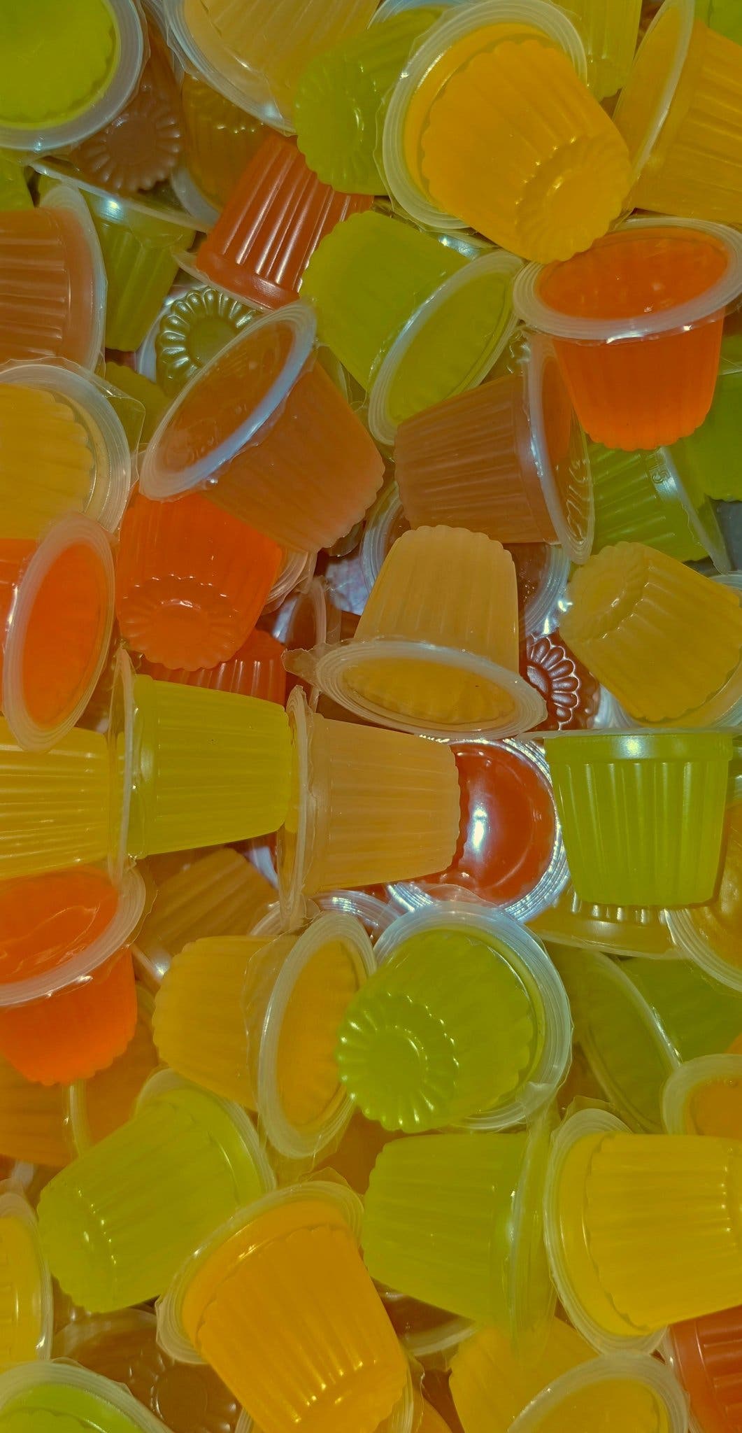 A pile of jelly pots in yellow, lime and orange, several tipped to show their ridged plastic cups.