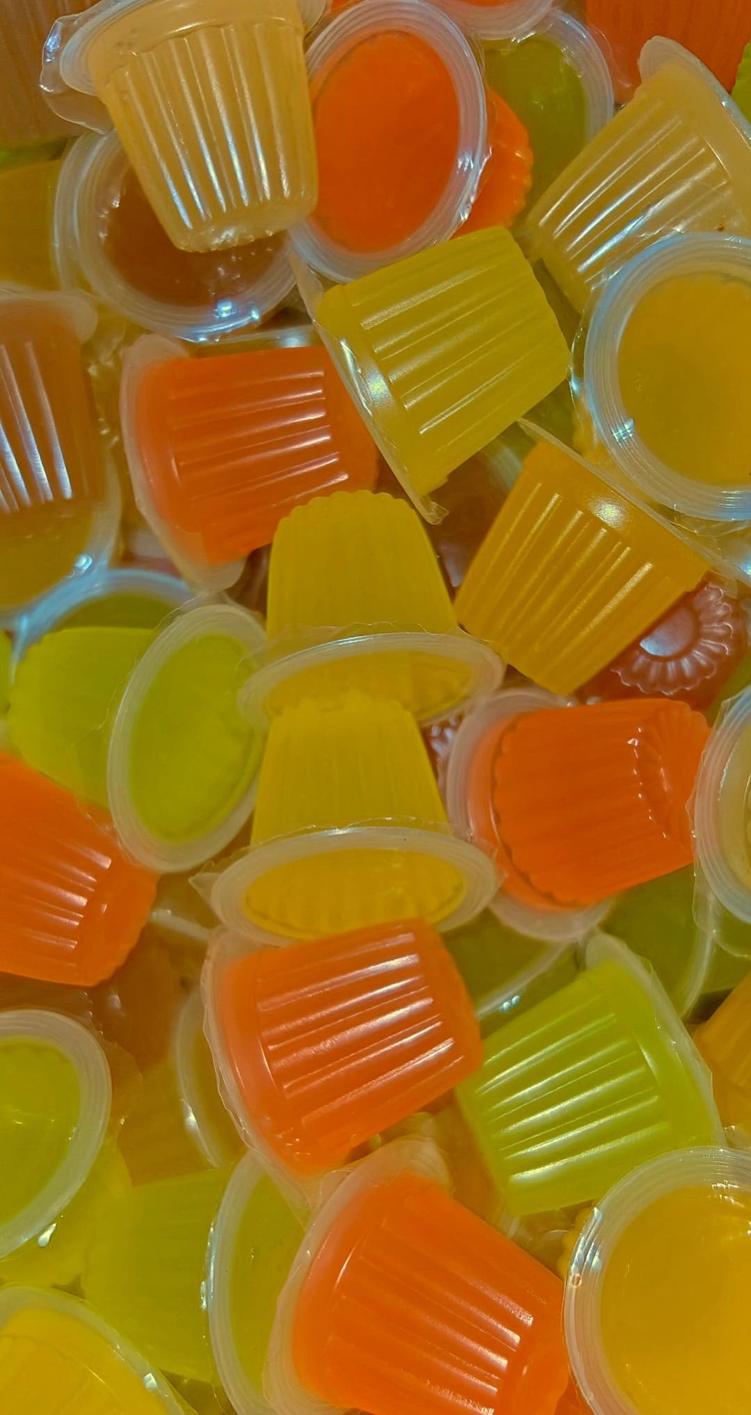 A dense heap of orange, yellow and lime jelly pots with their ridged sides uppermost.