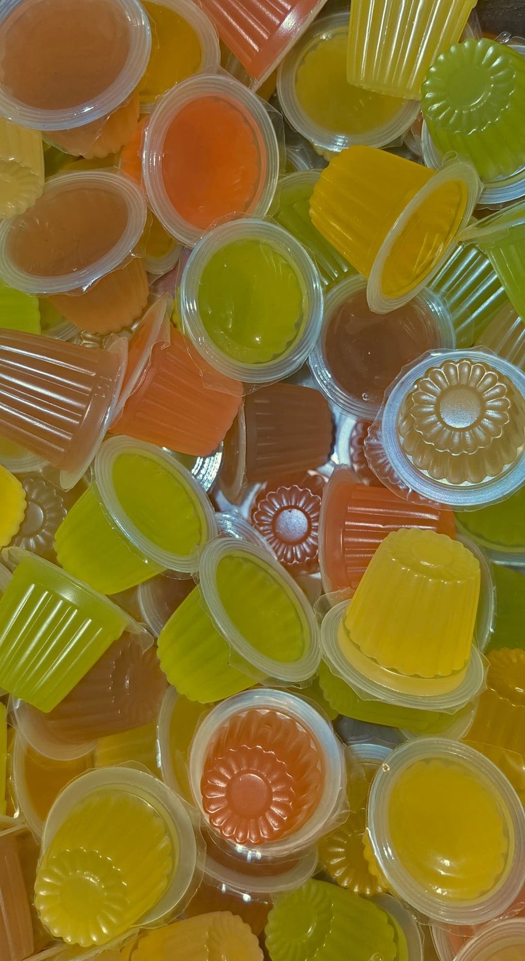 Jelly pots in yellow, green, orange and brown, several showing the flower shape pressed into the cup.
