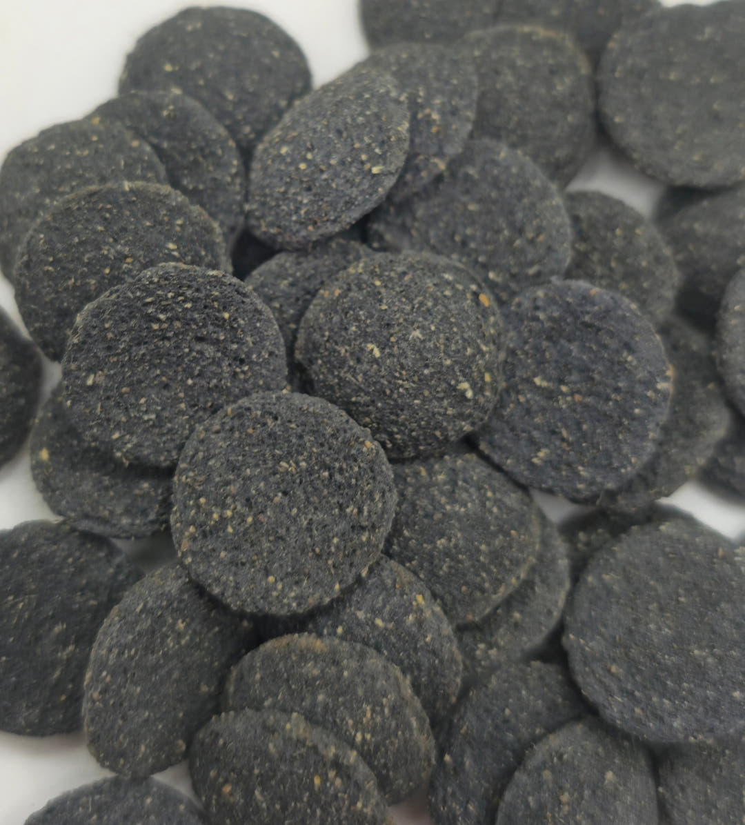 Close view of Oak and Algae wafers filling the frame, flat discs pitted and flecked with cream grains.