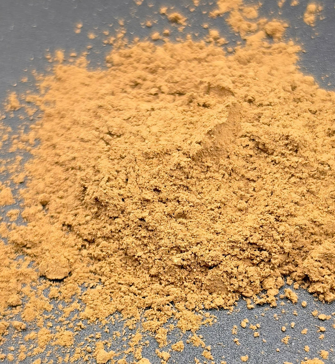 A mound of golden-brown mushroom blend powder on grey, with fine dust flicked out around it.