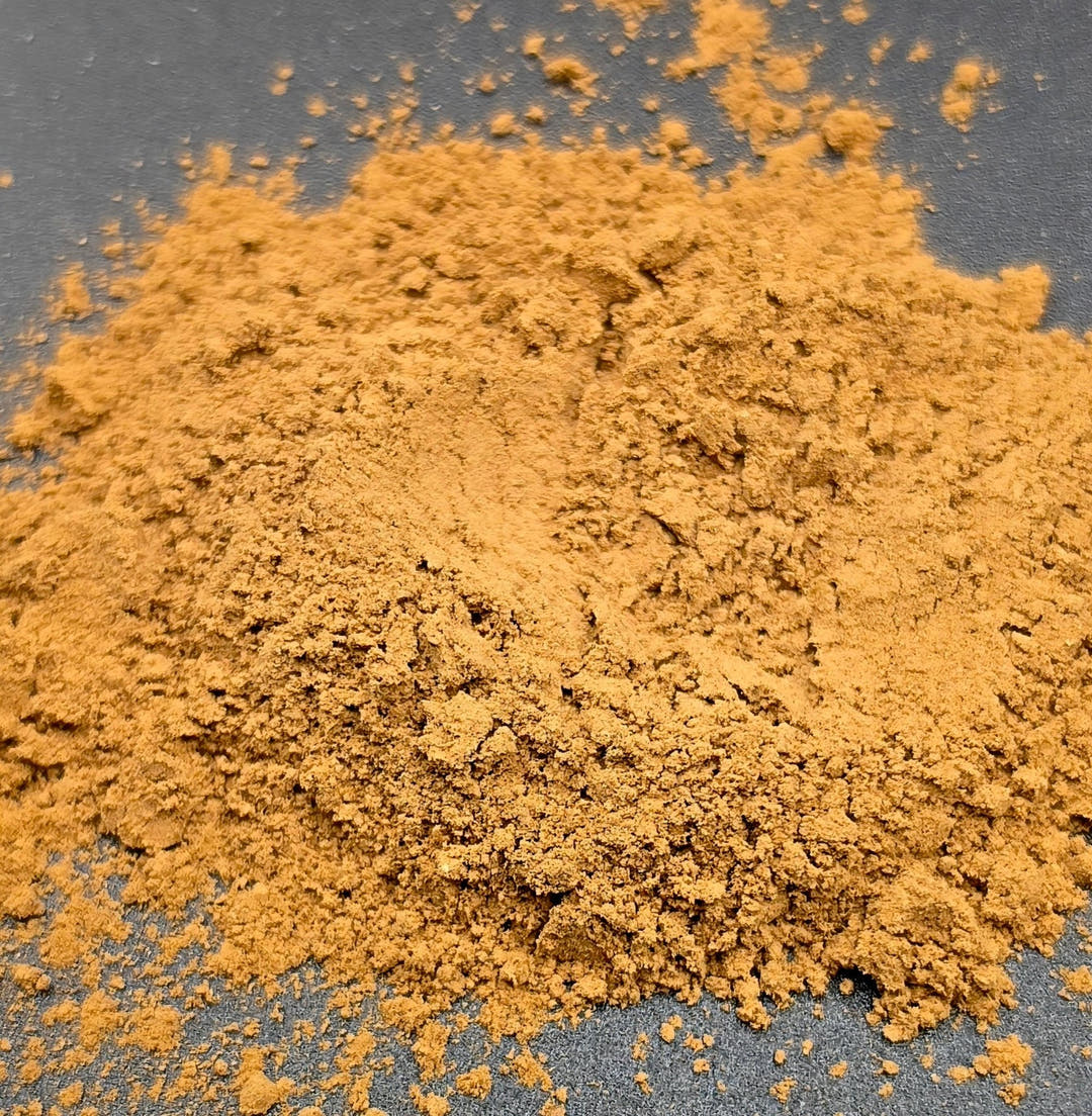 A heaped pile of orange-brown mushroom blend powder, its surface fine and floury, on dark grey.