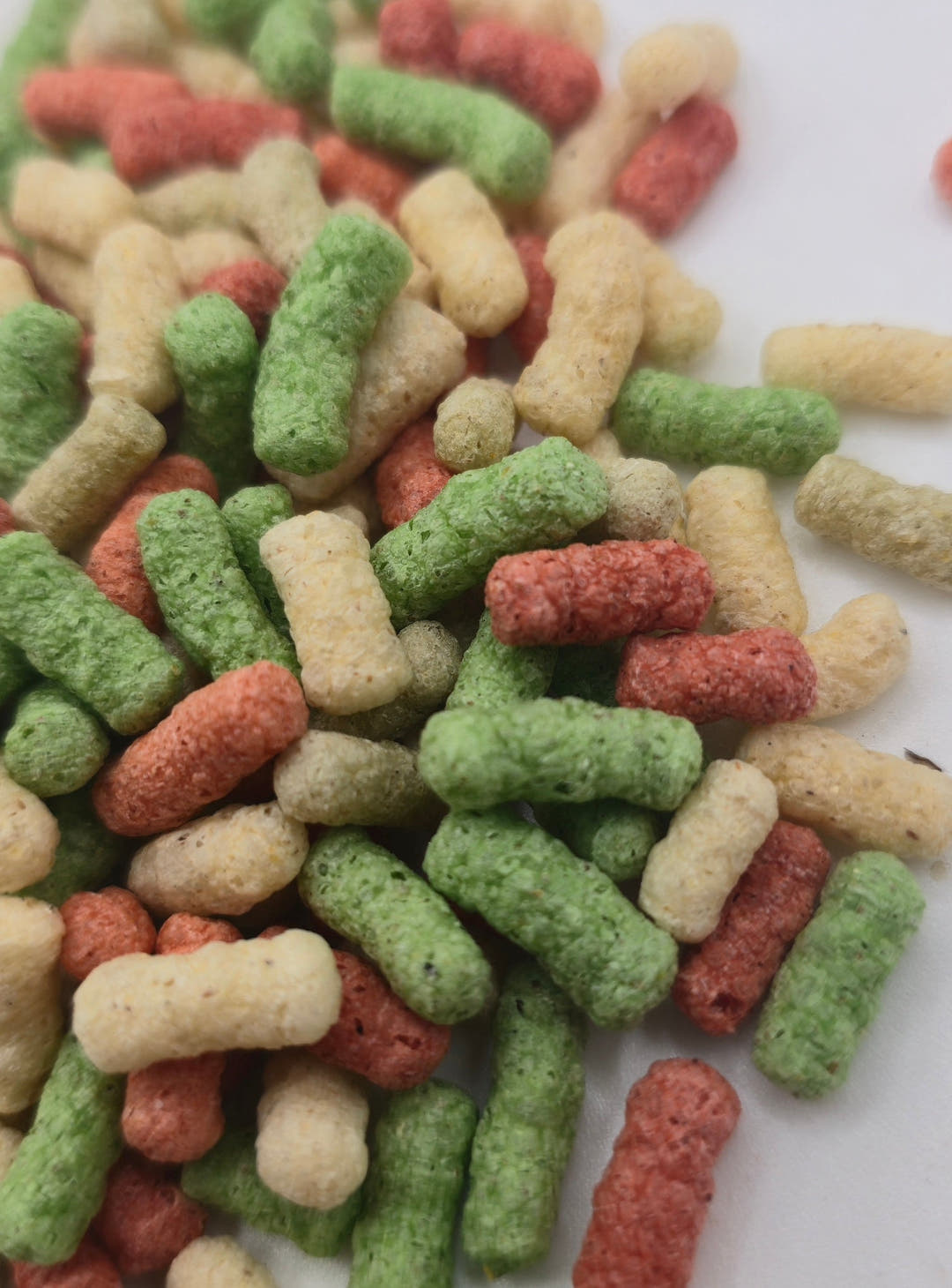 A loose pile of red, green and cream pond sticks on white, a few strays scattered off to one side.