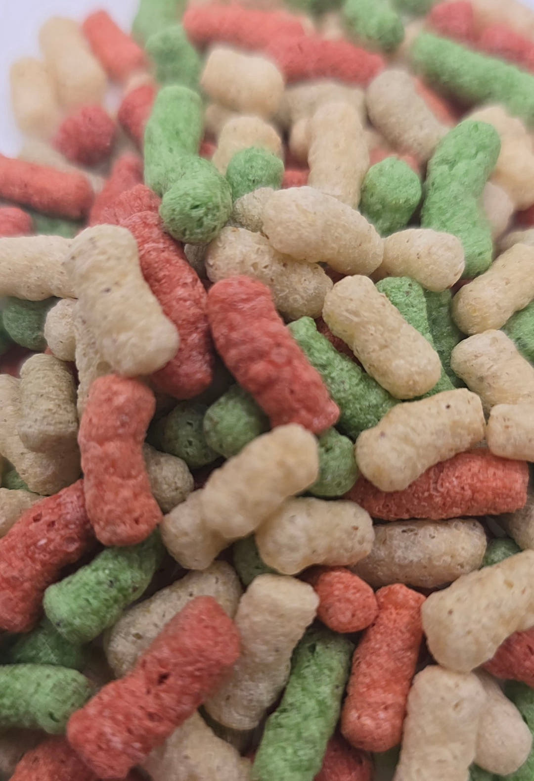 A heap of pond sticks filling the frame, cream, red and green pellets with a rough crumbly surface.