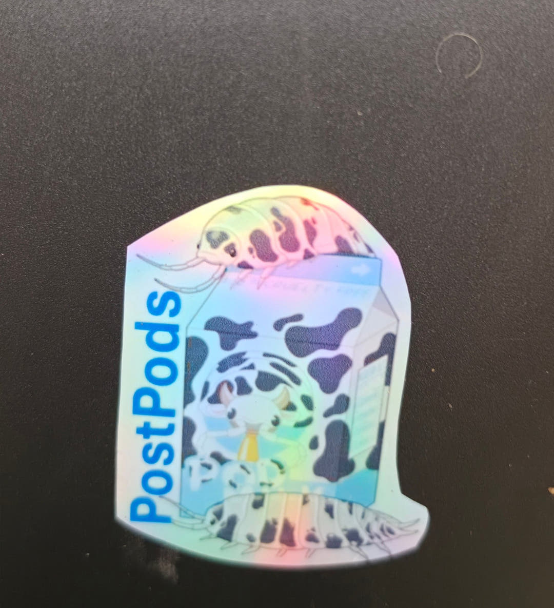 Sticker of a cow patterned milk carton reading PostPods, with matching black and white isopods above and below.