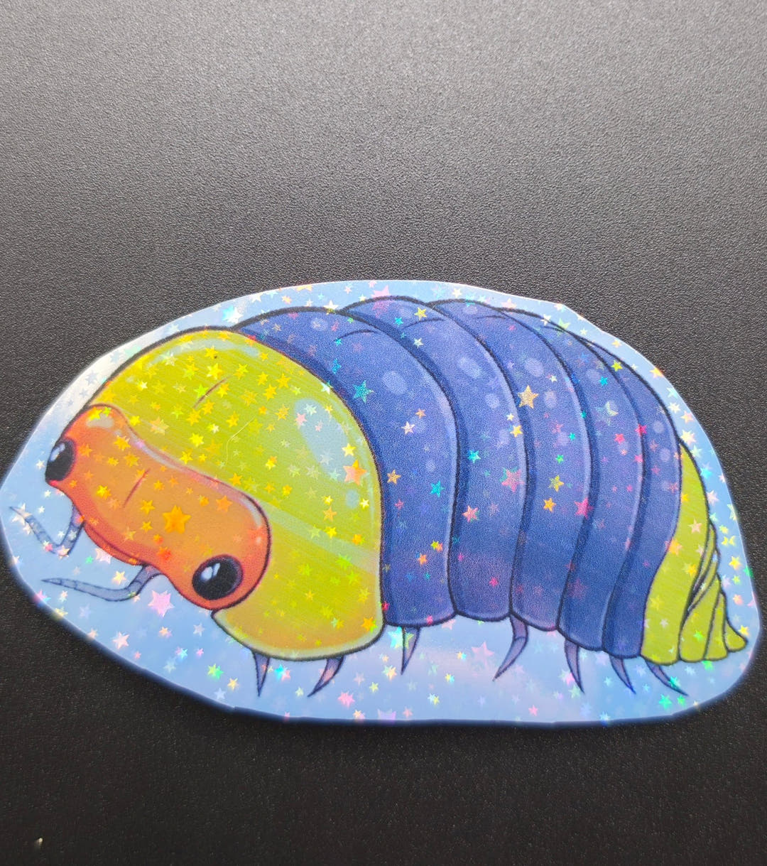 A vinyl sticker of a cartoon isopod with an orange face, yellow head shield and blue-purple back.
