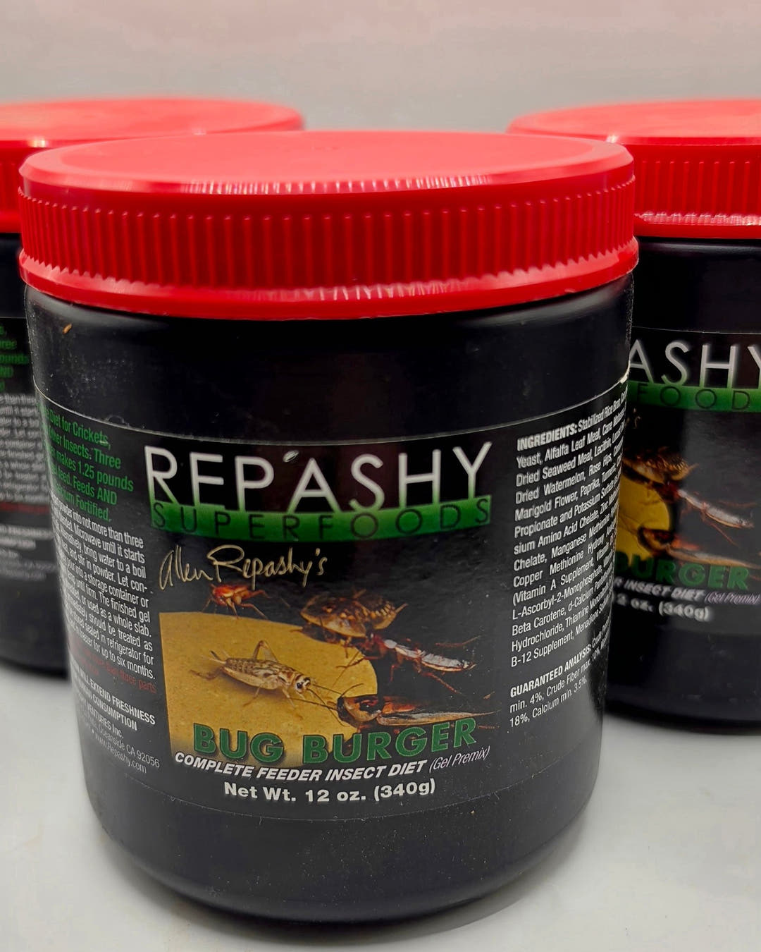 A 12 oz 340g Repashy Bug Burger jar with a red lid in front of two more, its front label facing out.