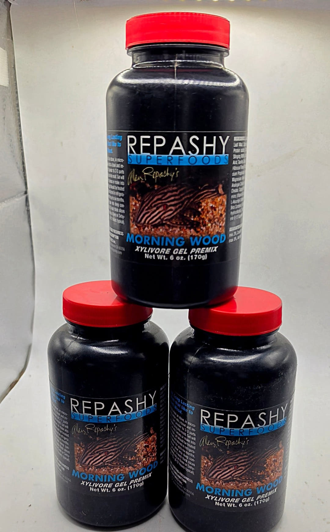 Three 6 oz Repashy Morning Wood jars in a triangle, red lids above dark labels carrying a catfish photo.
