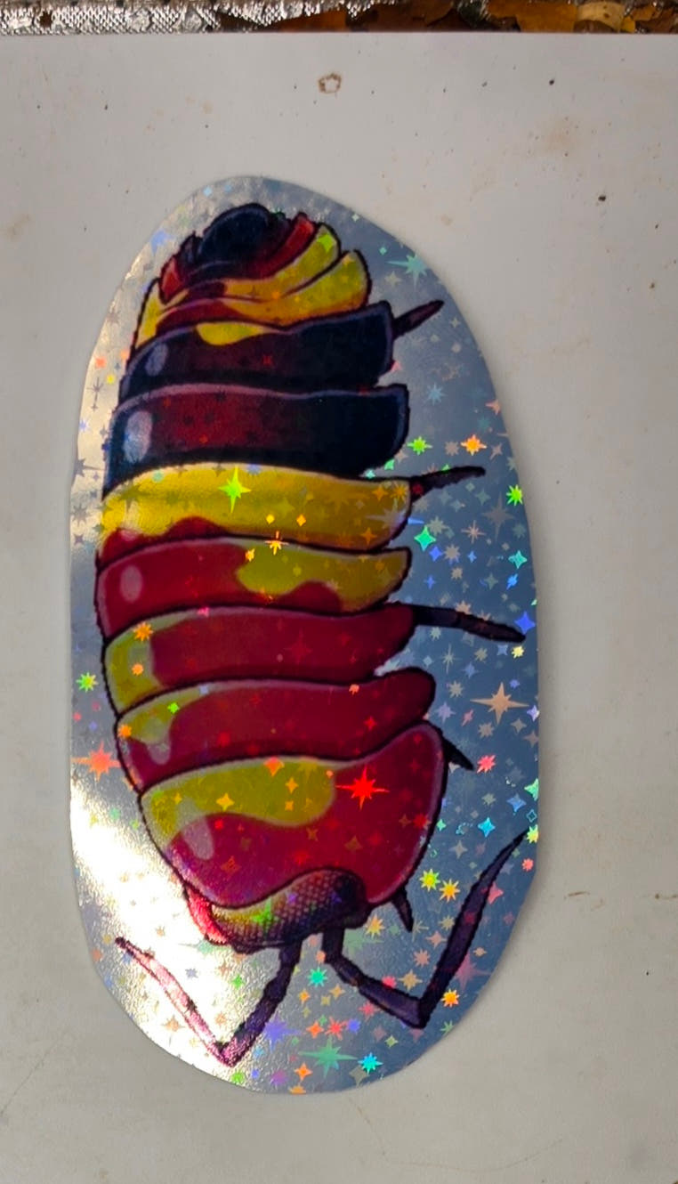 Scarlet isopod sticker: a curled crimson isopod splashed with yellow and banded with deep navy, on holographic star vinyl.