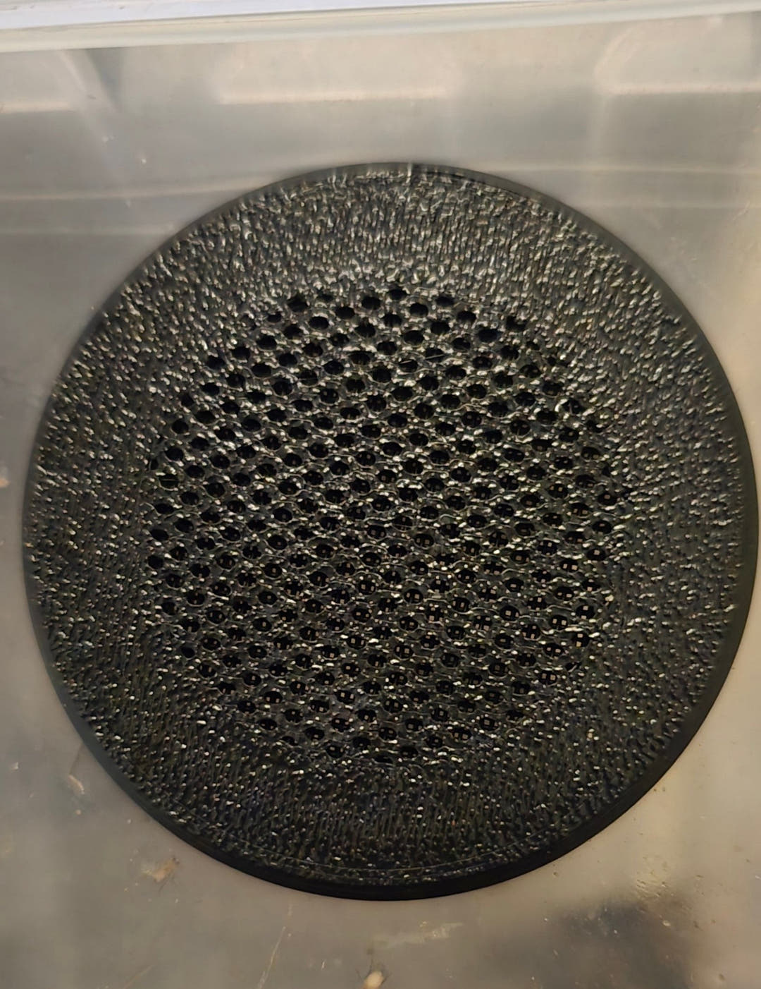 Close view of a screw-in air vent's mesh face, fitted into the wall of a clear tub.