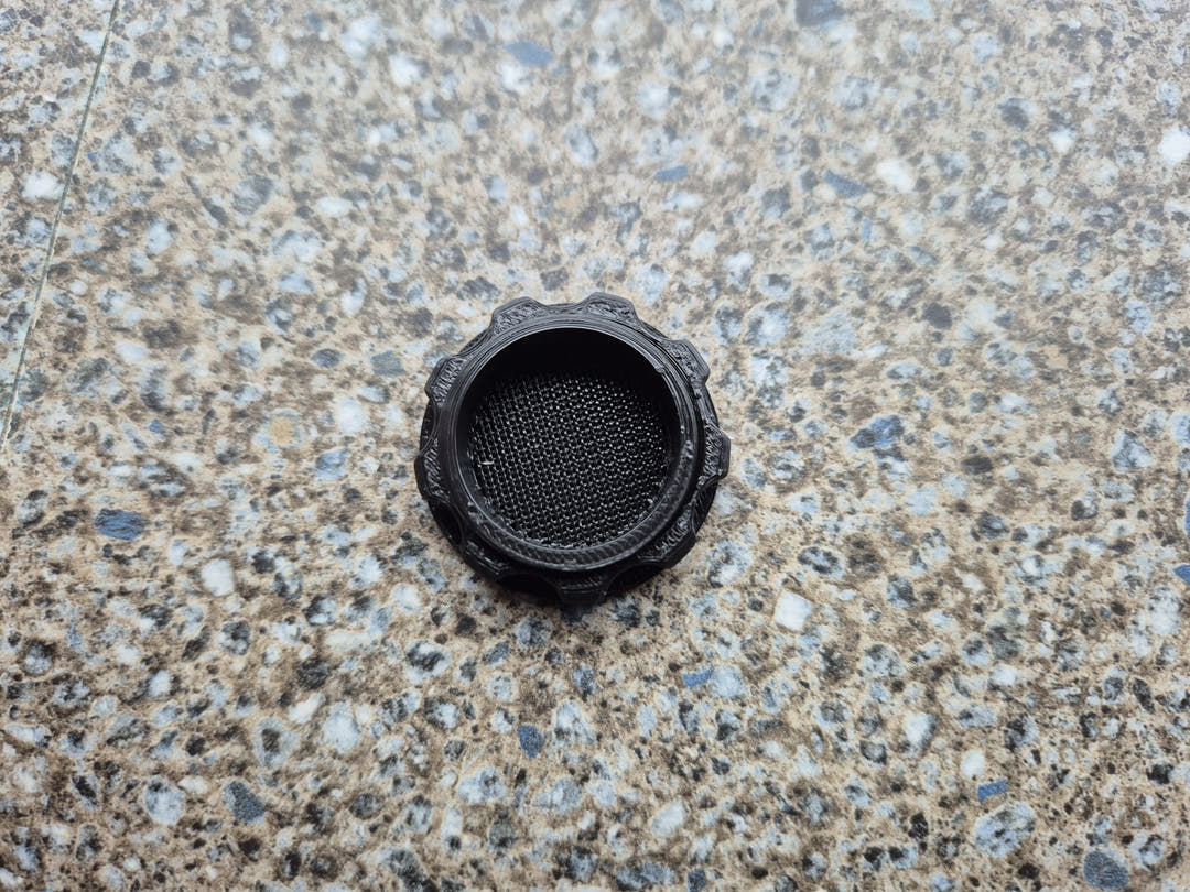 A single black screw-in air vent with fine mesh, photographed on a speckled worktop.