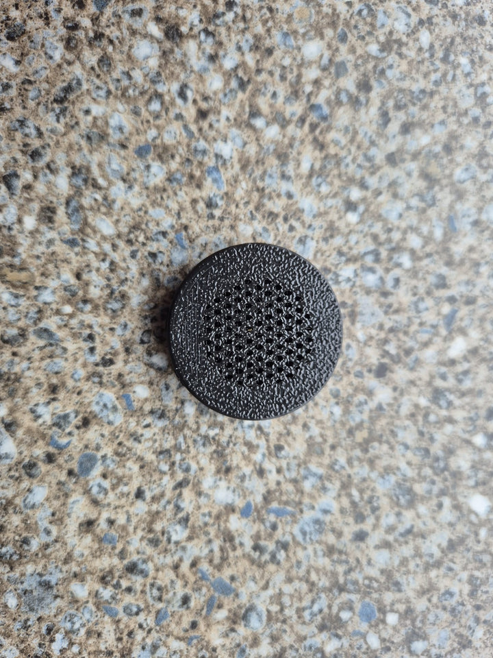 A screw-in air vent seen from directly above on a speckled worktop.