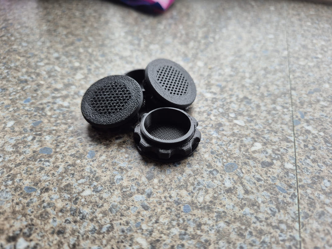 Three black screw-in air vents on a speckled worktop, two mesh faces up and one showing its threaded collar.