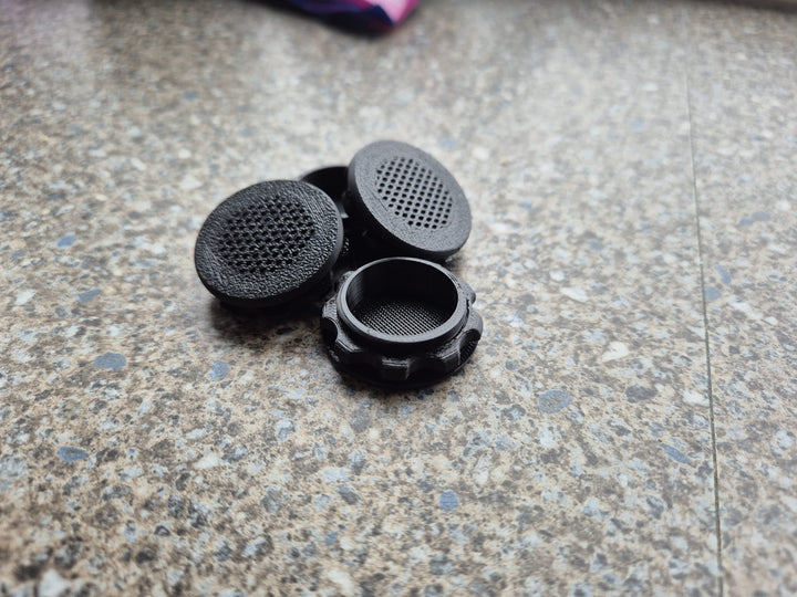 Three black screw-in air vents on a speckled worktop, two mesh faces up and one showing its threaded collar.