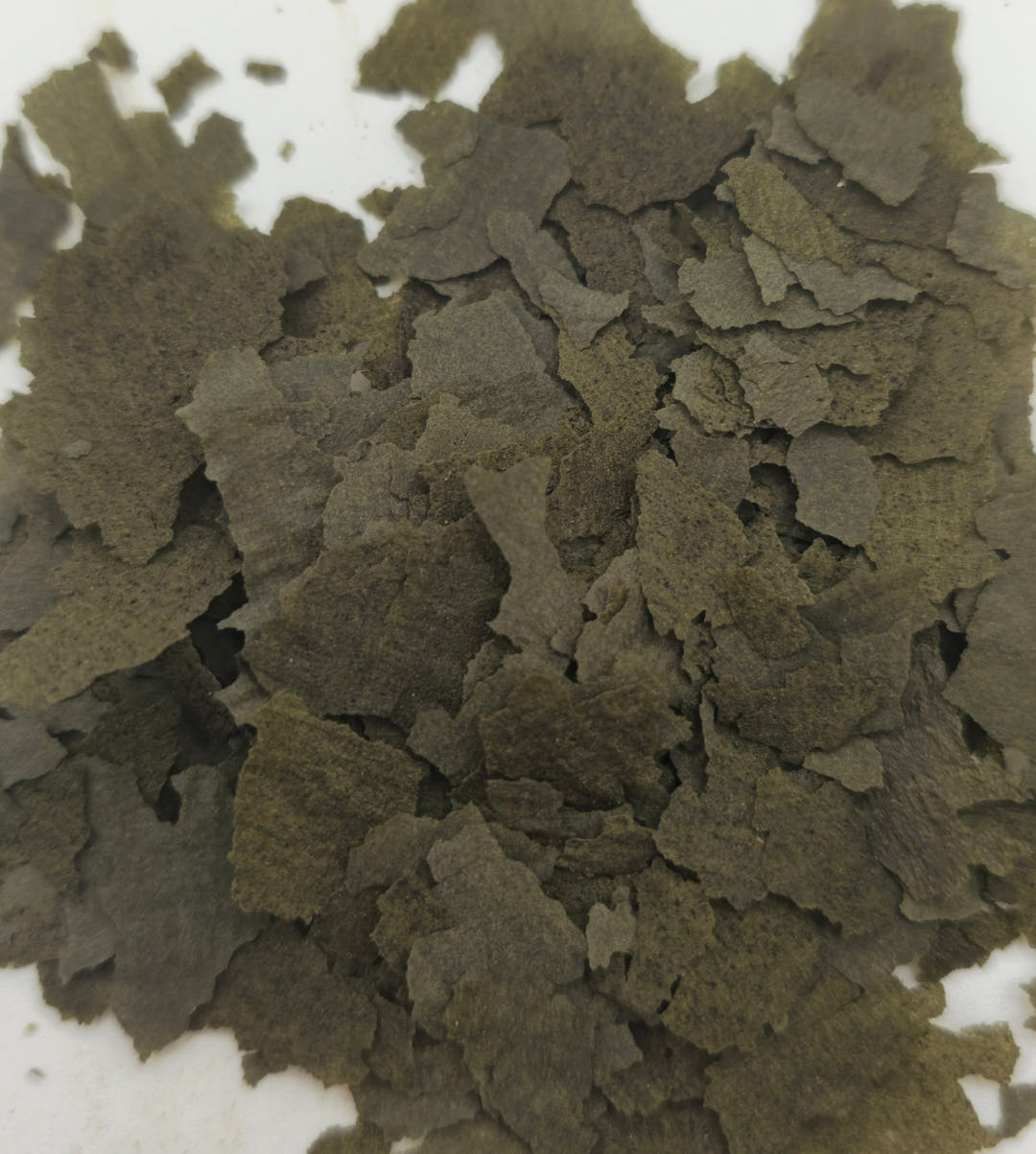 A loose pile of ragged green-grey flakes, thin and papery, with white showing around the edges.