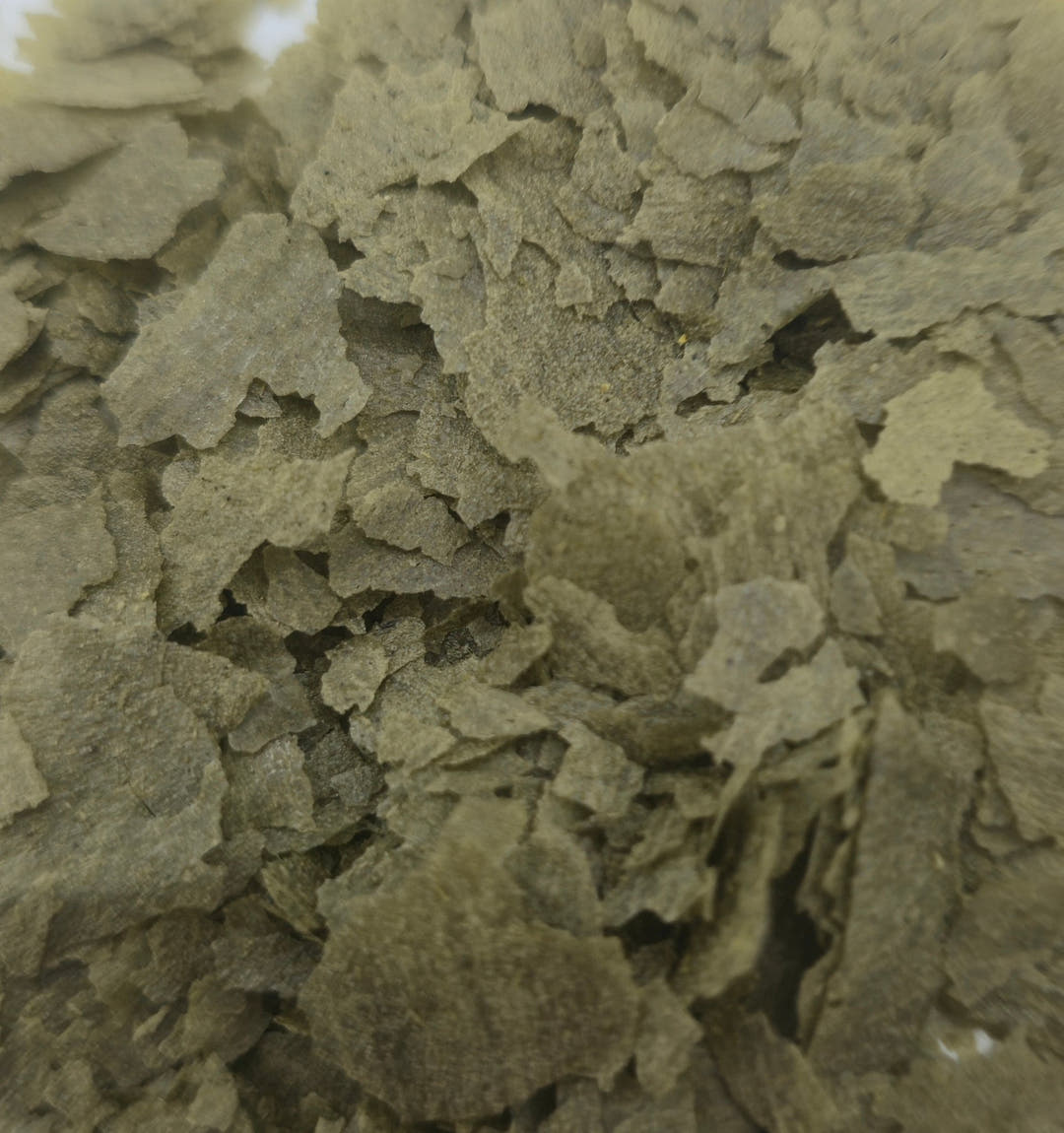 Khaki green vegetable flakes filling the frame, thin dry pieces with torn ragged edges.